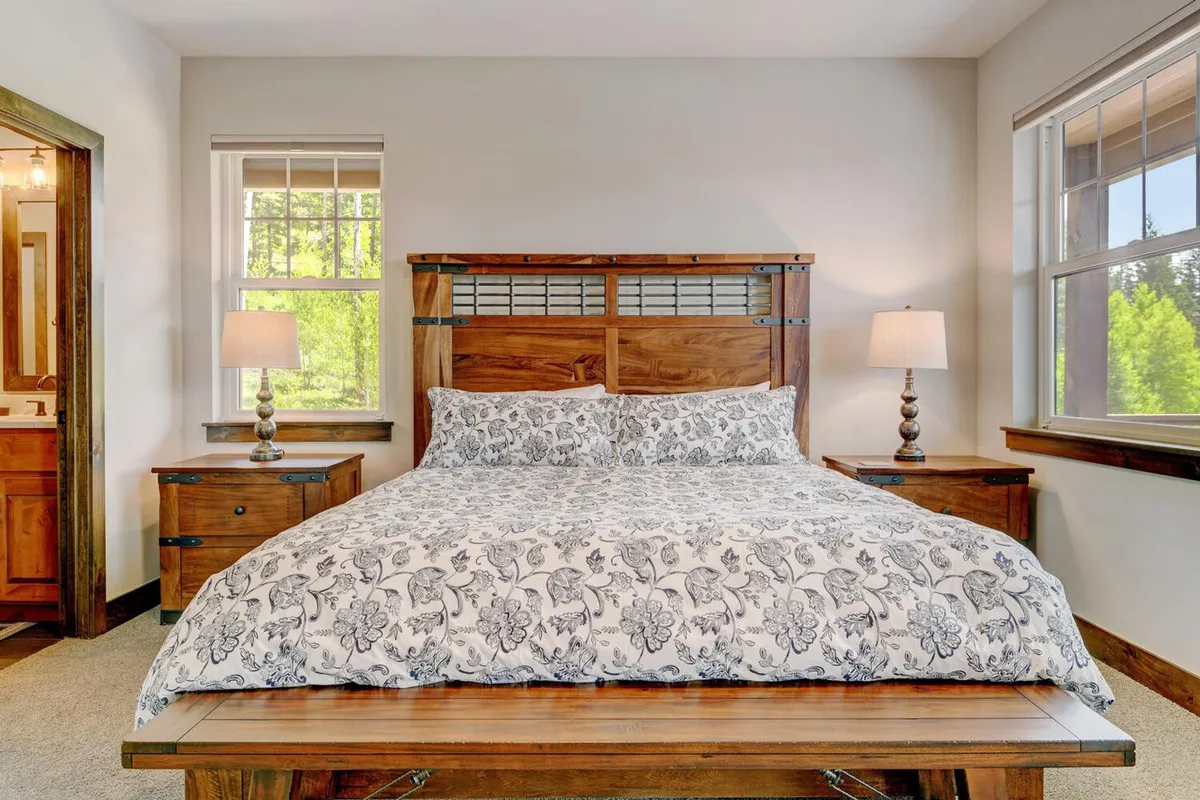 A tranquil bedroom with a wooden bed frame, floral patterned bedding, and warm table lamps. The space is bathed in soft, natural light, creating a serene sanctuary ideal for relaxation and restful sleep.