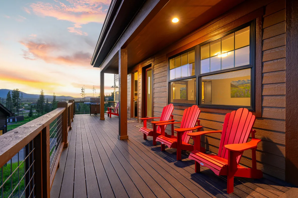 An inviting wooden deck is adorned with classic red Adirondack chairs facing a sunset sky. The scene exudes tranquility and encourages guests to relax, socialize, and enjoy panoramic mountain views from the comfort of the home's outdoor spaces.