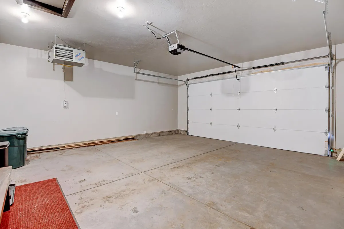 An interior view of the heated garage with a clean concrete floor, prominent garage door, and ample ceiling lights. The uncluttered space is ideal for storing outdoor gear such as bikes and skis, highlighting the practical side of adventure transitions.