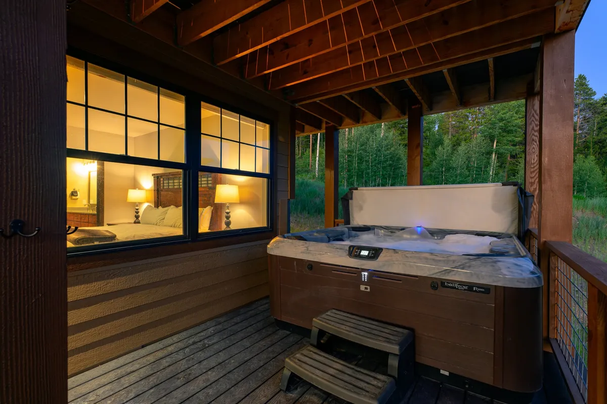 This exterior image features a private hot tub nestled beside the home, with lush greenery surrounding the space and a nearby bedroom window. The tranquil setting is perfect for relaxation and intimate moments, especially after a day of adventure.