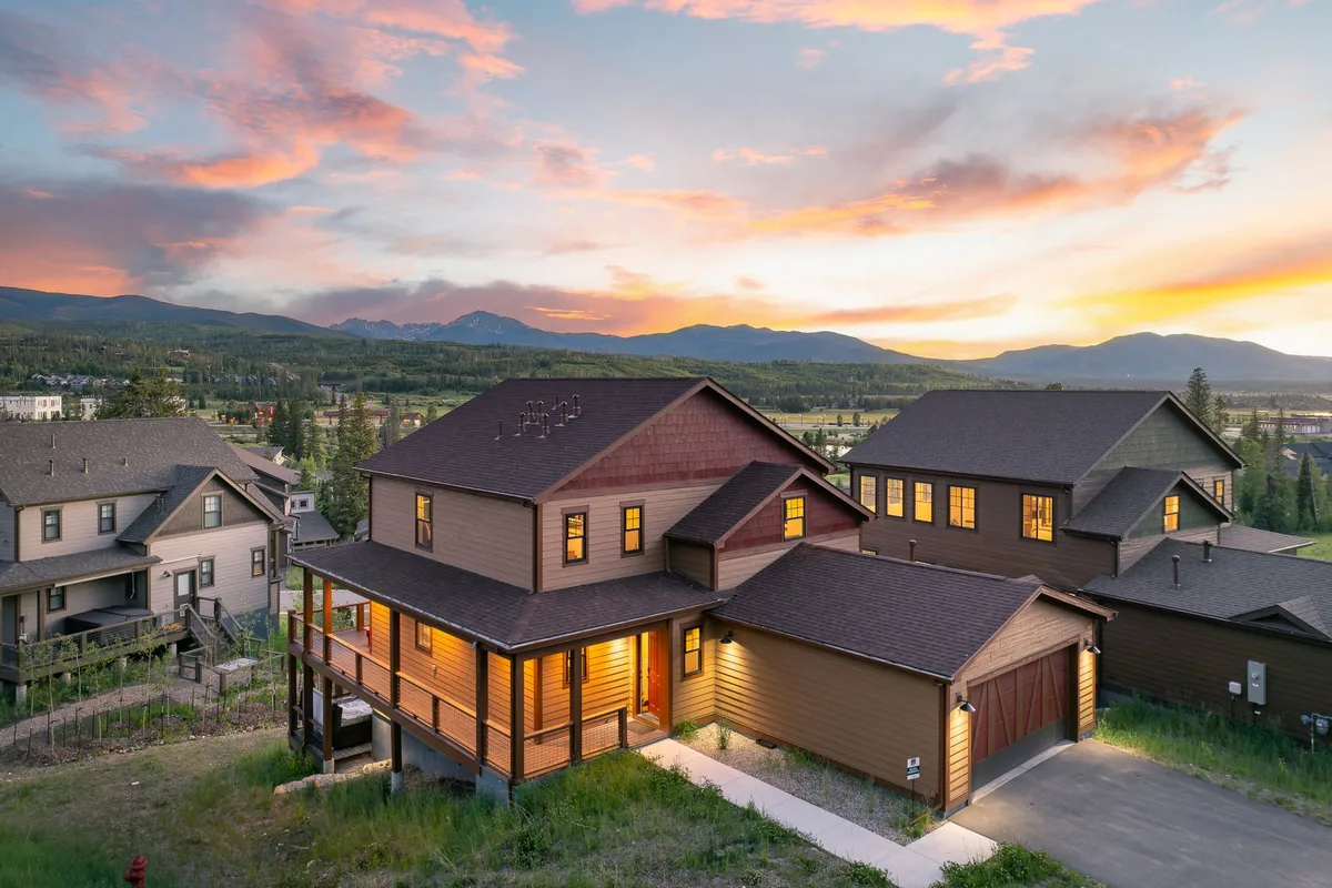 The hero image displays a luxurious chalet glowing warmly at dusk, nestled in the Colorado mountains. The sky is ablaze with vibrant sunset colors, and the house’s inviting lights spill onto a spacious porch, hinting at gatherings, relaxation, and memorable evenings. Majestic mountains and open landscapes surround the scene, reinforcing a sense of serenity and outdoor adventure.